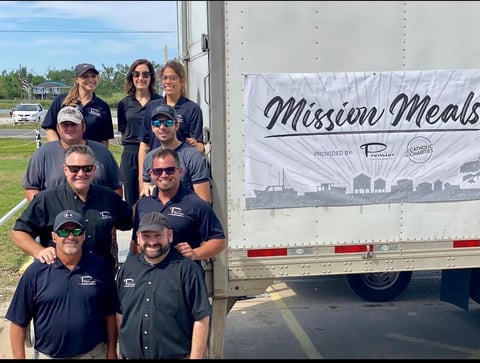 Group of seven people in dark blue polo shirts standing in front of a Mission Meals food truck trailer
